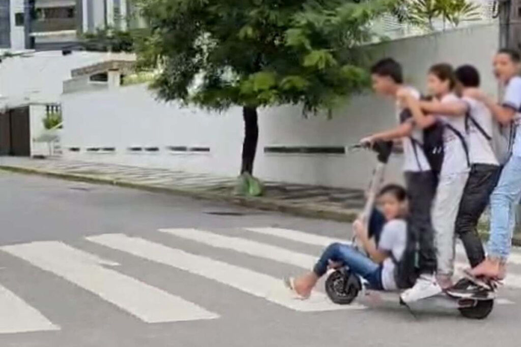 IMAGEM MOSTRA CINCO JOVENS NA MESMA PATINETE ELÉTRICA EM BOA VIAGEM, NO RECIFE.