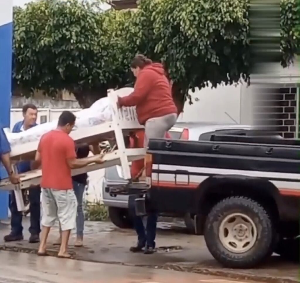 Homem acamado é levado em caminhonete, sob chuva, para emitir documento em Palmeira dos Índios.